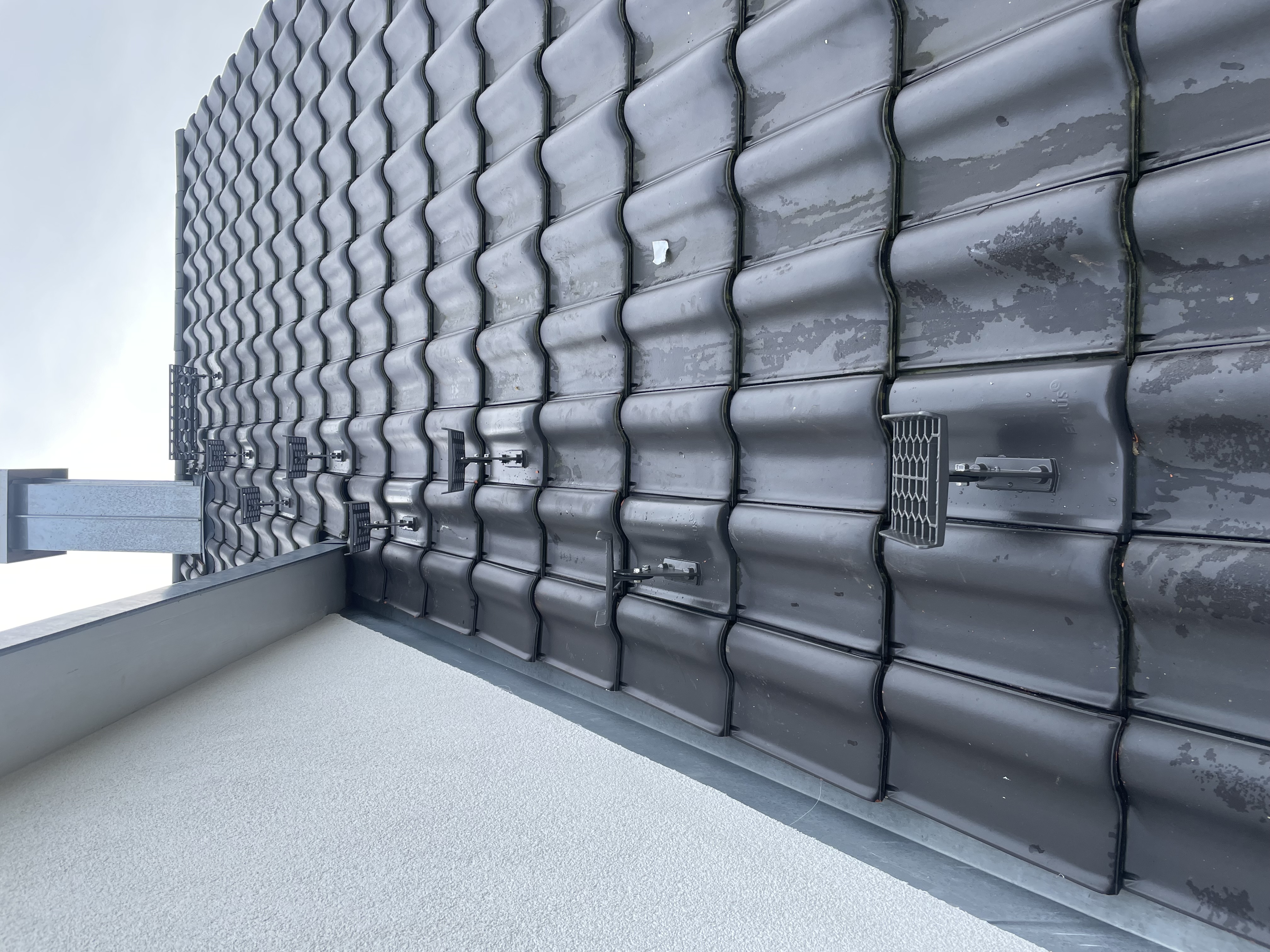 Nahaufnahme eines modern eingedeckten Daches mit dunklen Ziegeln und Schneefanggitter